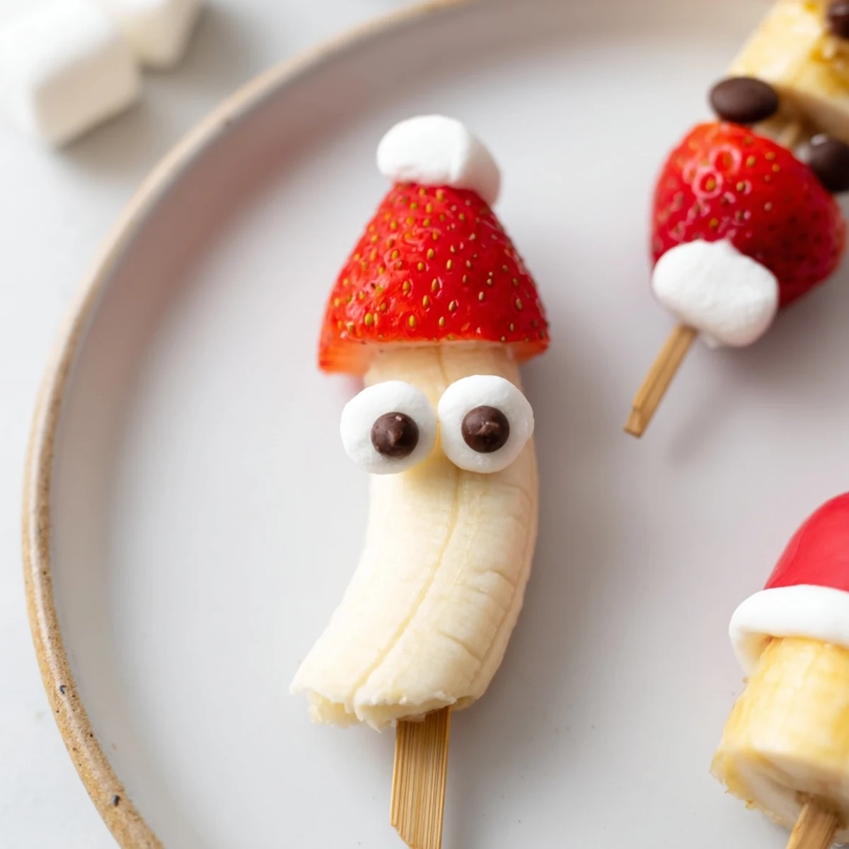 Sweet, assembled Banana Strawberry Santa Skewers with banana "faces" and marshmallow hats, ready to eat.
