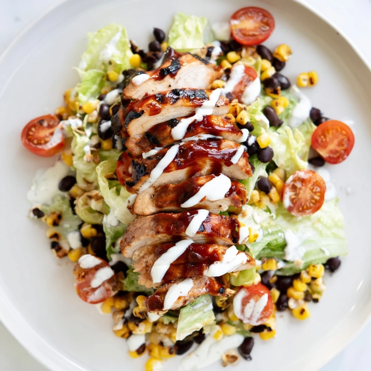 Smoky BBQ chicken slices rest on crisp romaine with grilled corn and black beans, all drizzled with creamy ranch dressing.  