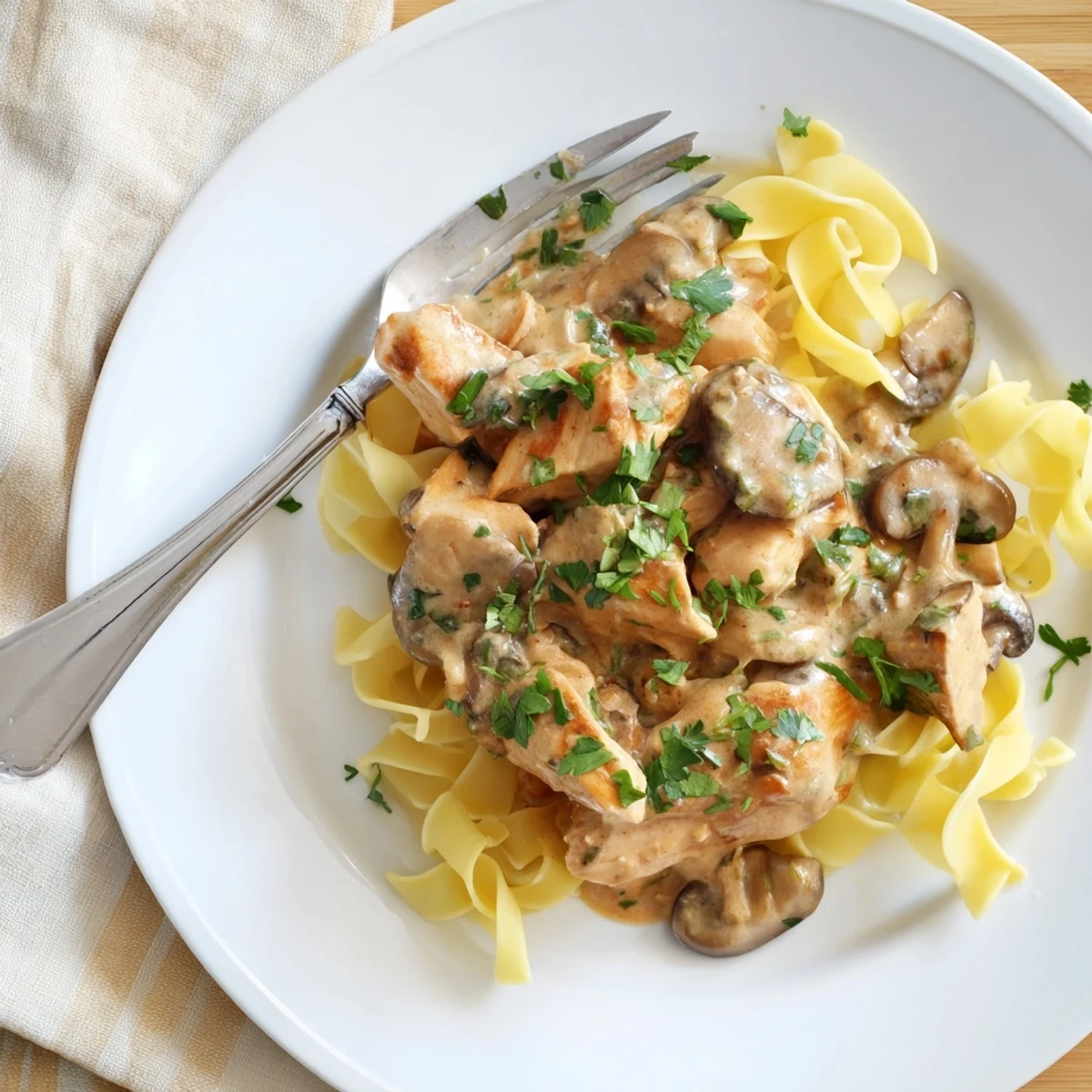 A close-up of chicken and mushroom stroganoff on a white plate, garnished with fresh parsley, showing a rich, creamy texture.