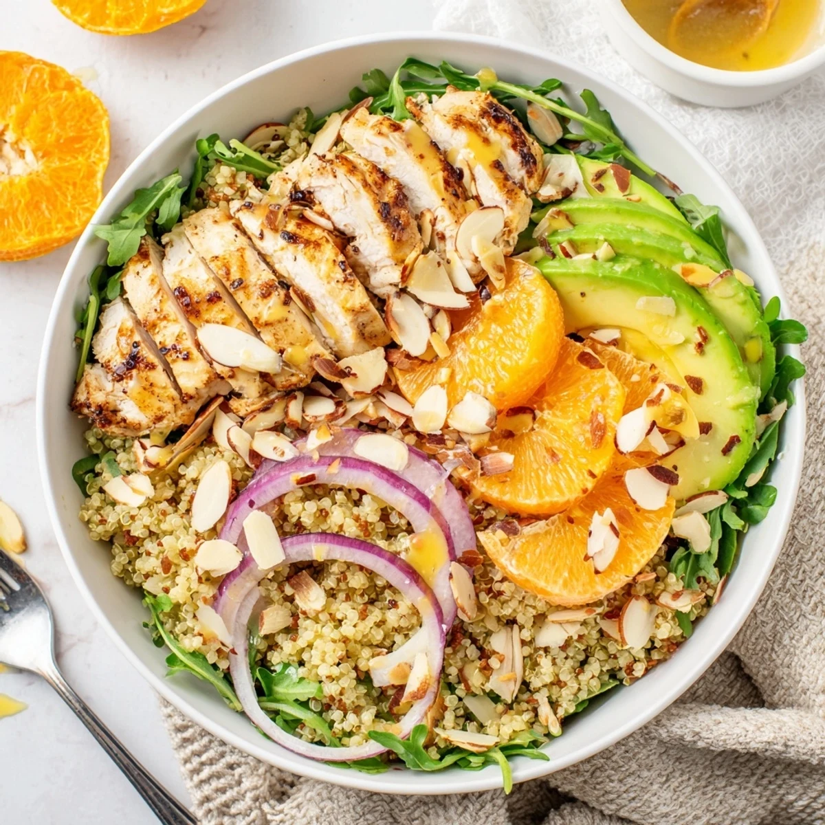 Sliced herb-grilled chicken rests atop a vibrant bowl of citrus herb chicken salad with quinoa, avocado, and toasted almonds.