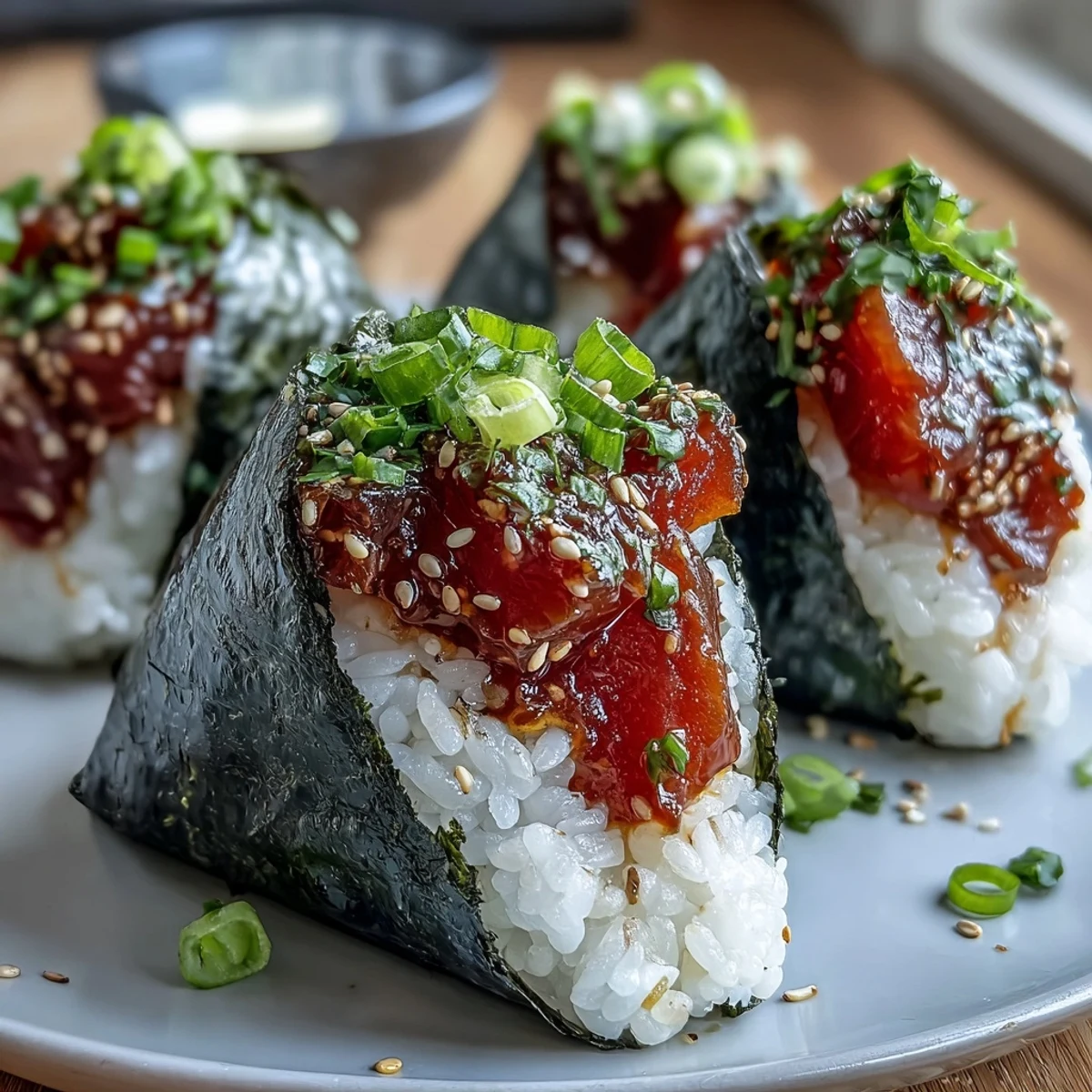 Hand-shaped onigiri rice balls featuring spicy tuna filling, nori wrap, and vibrant green onion garnish.