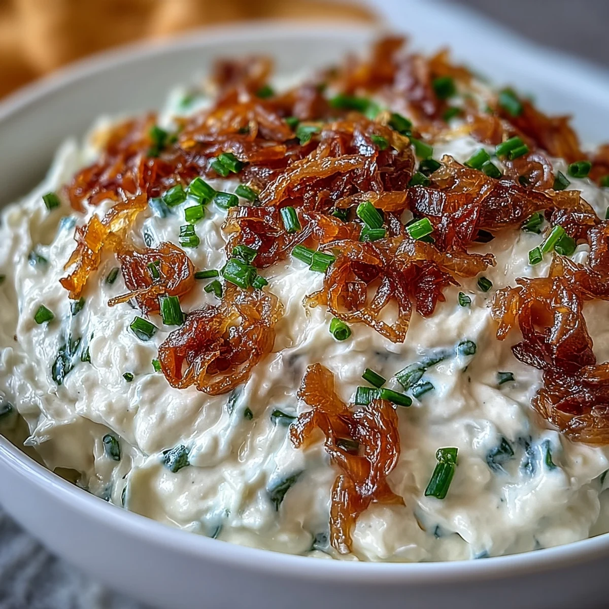 Rich, golden caramelized onions blended into tangy sour cream dip, garnished with fresh chives for a savory appetizer spread.