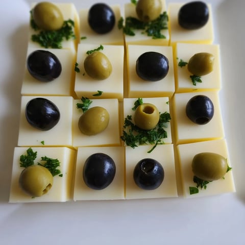 A composed Cheese and Olive Chess Board: cheddar and mozzarella squares with black and green olives ready to be served.