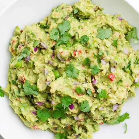 Creamy Edamame Guacamole, a vibrant appetizer, garnished with fresh cilantro and served with lime wedges.