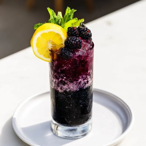 Dark Matter Mocktail, layered and inky black, a visually stunning non-alcoholic drink with vibrant garnishes.