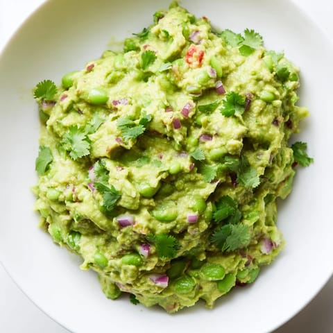 Fresh, homemade Edamame Guacamole with visible chunks of tomato, is ready to be scooped up with chips.