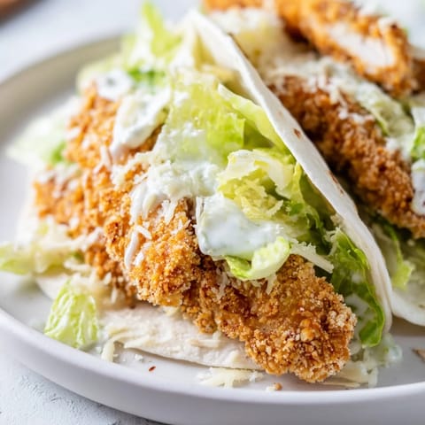 Sliced Crispy Chicken Caesar Wrap on a plate, drizzled with creamy dressing and served with lemon wedges.